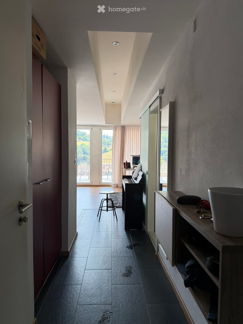 Hallway leading to a room with a piano, stool, small table, and chair. Cabinet with a vase on top and shelves below.