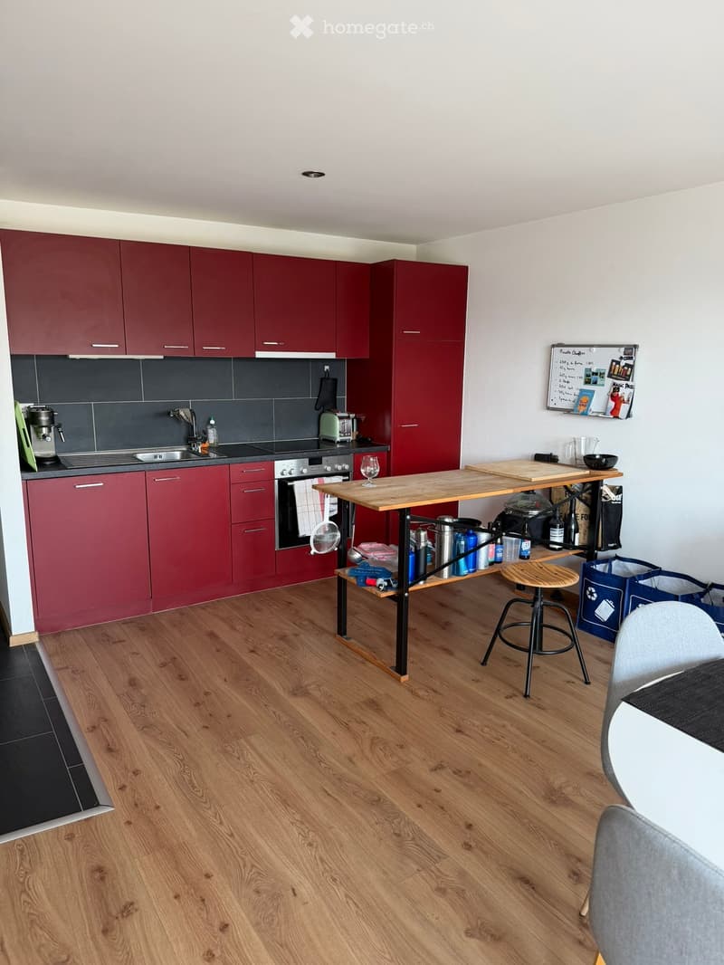 Modern kitchen with red cabinets, wooden floor, sink, oven, coffee maker, toaster, and a wooden cutting board on a table.