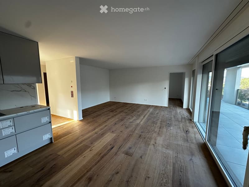 Empty room with wooden flooring, white walls, and large windows leading to a balcony area.