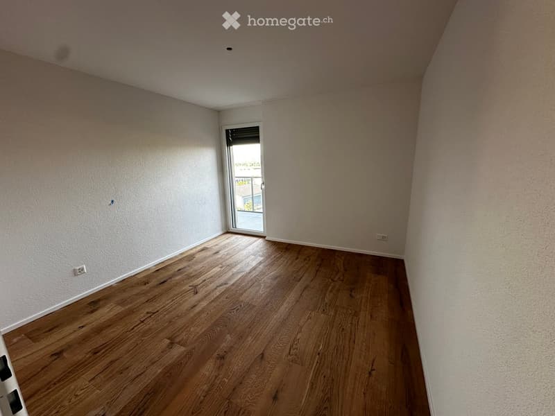 Empty room with wooden flooring and white walls, featuring a sliding glass door leading to an outdoor area.
