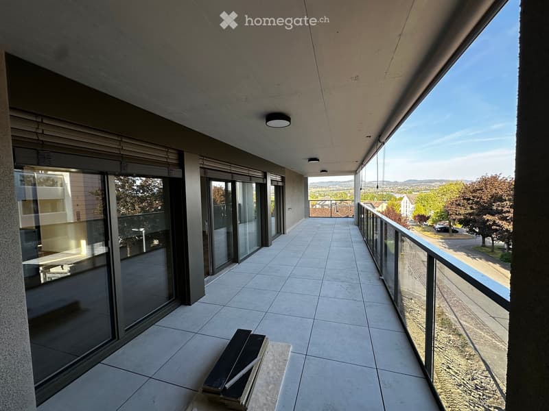Modern balcony with tiled floor, large glass sliding doors, metal railing, and scenic view of the surrounding area.