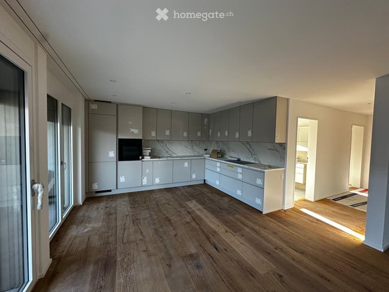 Modern kitchen with grey cabinets, marble countertop, and wooden flooring. Features an oven, sink, and ample cabinet space.