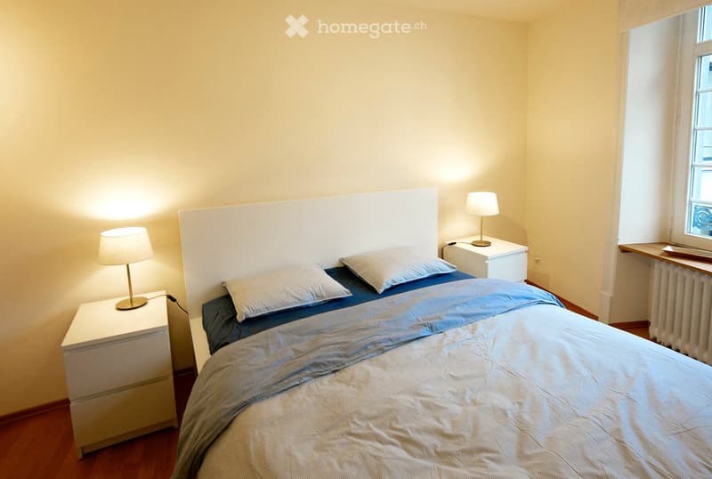 Queen bed, white headboard, bedside tables, bedside lamps, radiator, wooden floor