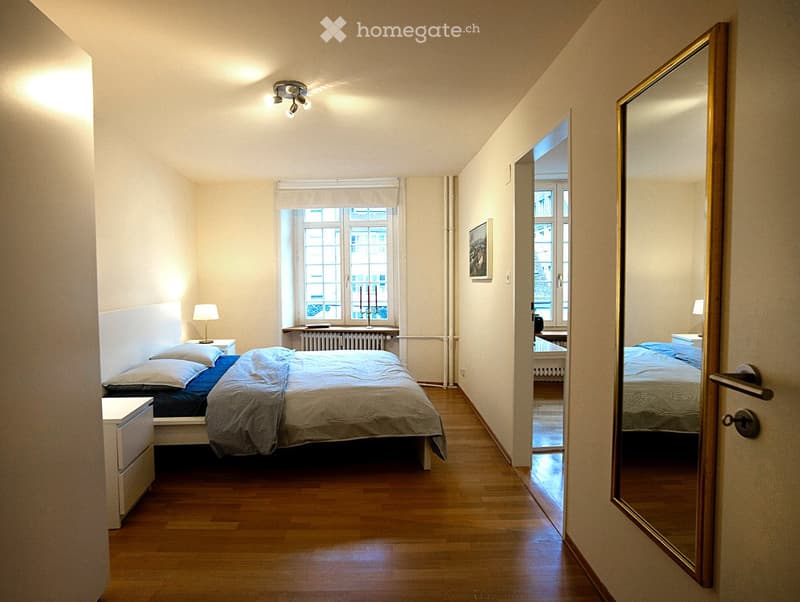 Bedroom with a bed, nightstand, lamps, mirror, and window