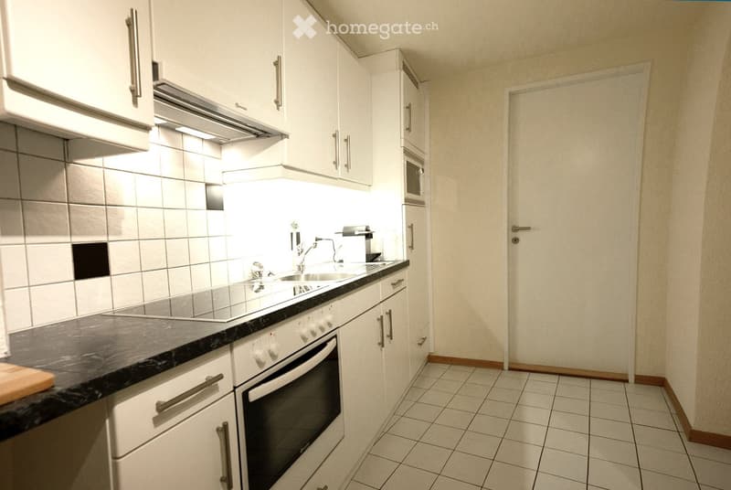 Modern kitchen with white cabinets, black countertop, stainless steel appliances, and a built-in range hood. Features a sink with a modern faucet, an oven, and a microwave.