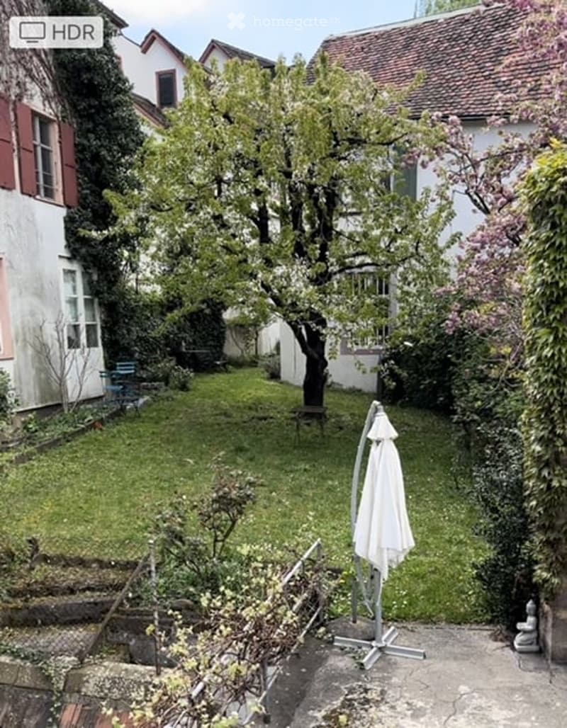 a garden with lawn, trees, shrubs, and a closed patio with furniture