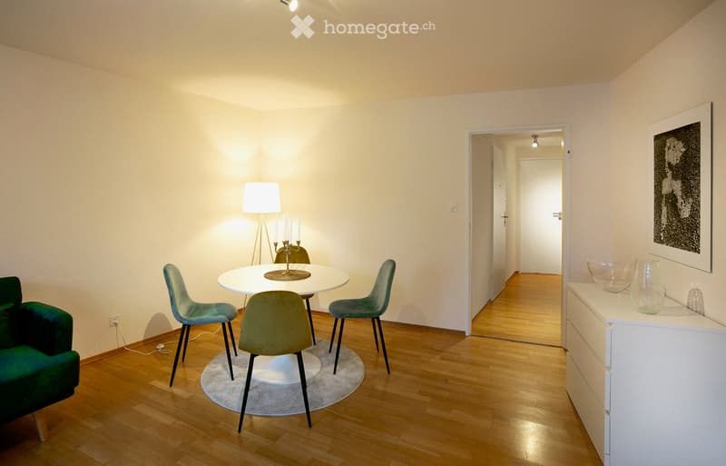 Small dining area with a round table, 4 chairs, lamp, green armchair, white sideboard, wall art, and a rug