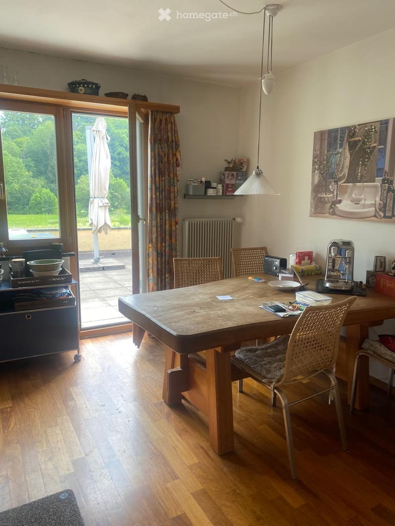 Bright kitchen with wooden flooring, large dining table, four chairs, built-in oven, fridge, coffee machine, and a view to the balcony.