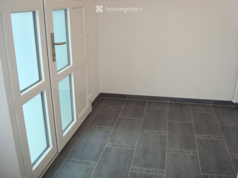 Empty hallway with grey tiled floor, white walls, and a white door with glass panels on the left side.