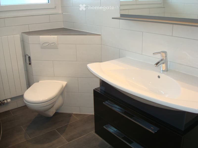 Modern bathroom with white tiles, a toilet, a sink with a chrome faucet, and a dark wooden cabinet.