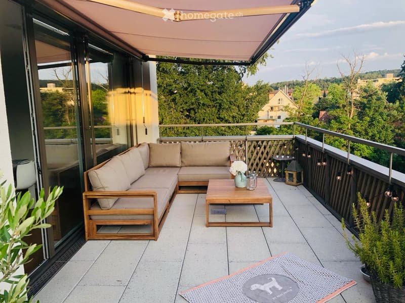Balcony with a sectional sofa, coffee table, and decorative items, overlooking a green landscape.