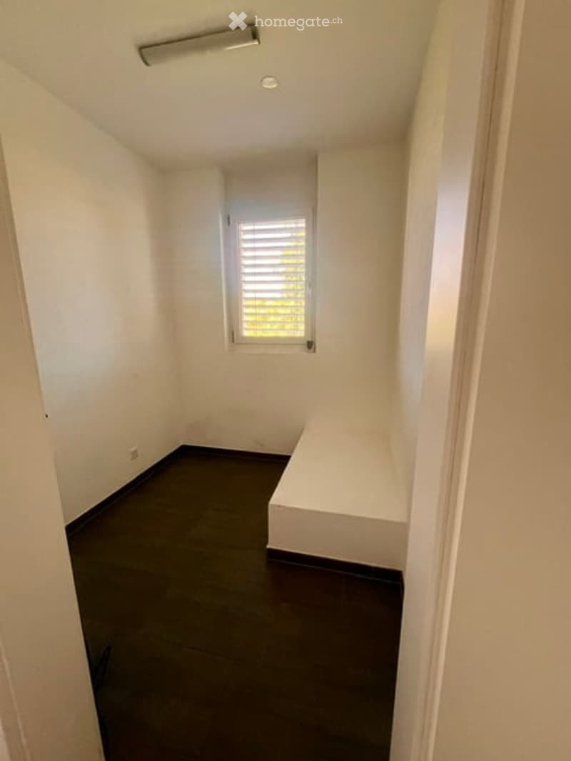 Empty room with white walls, dark flooring, and a single window with blinds. No furniture or equipment present.
