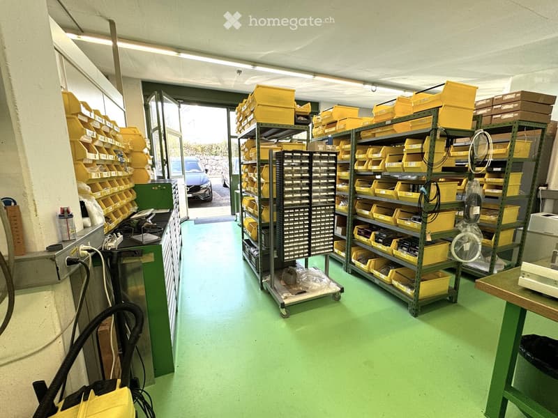 Warehouse with green floor, yellow storage boxes, shelves, trolleys, electrical outlets, and a car parked outside