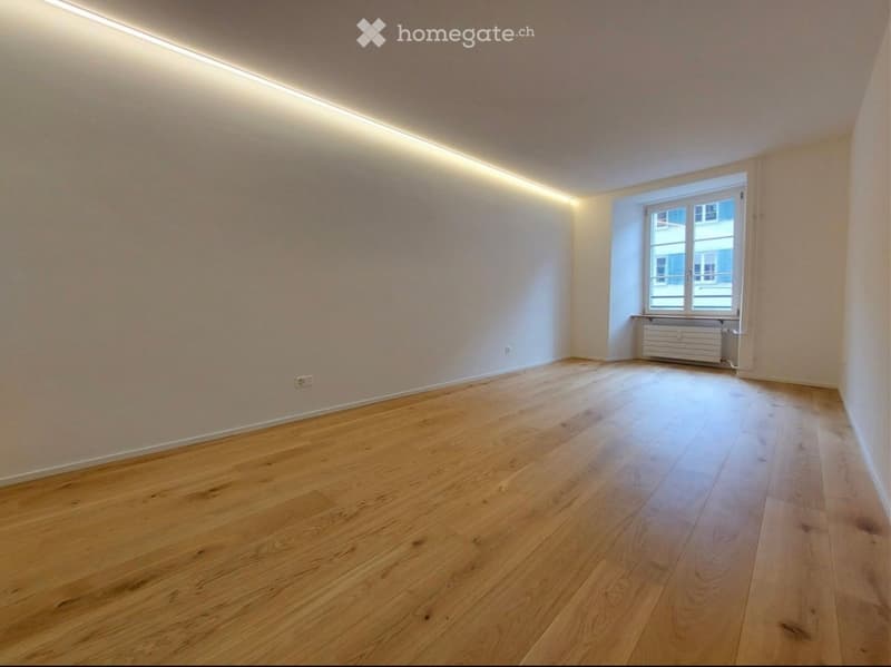 Empty room with wooden flooring, white walls, and a single window with a radiator below it.