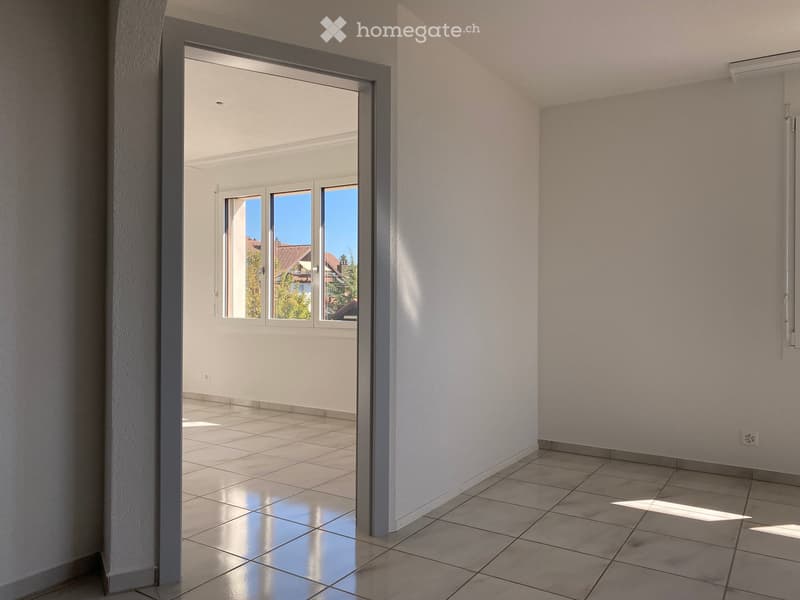 Empty room with tiled flooring and white walls, featuring an open doorway leading to a balcony with windows and a view of the outside area.