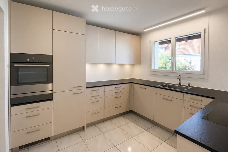 Modern kitchen with light-colored cabinets, stainless steel oven, black countertop, and a sink with a faucet.