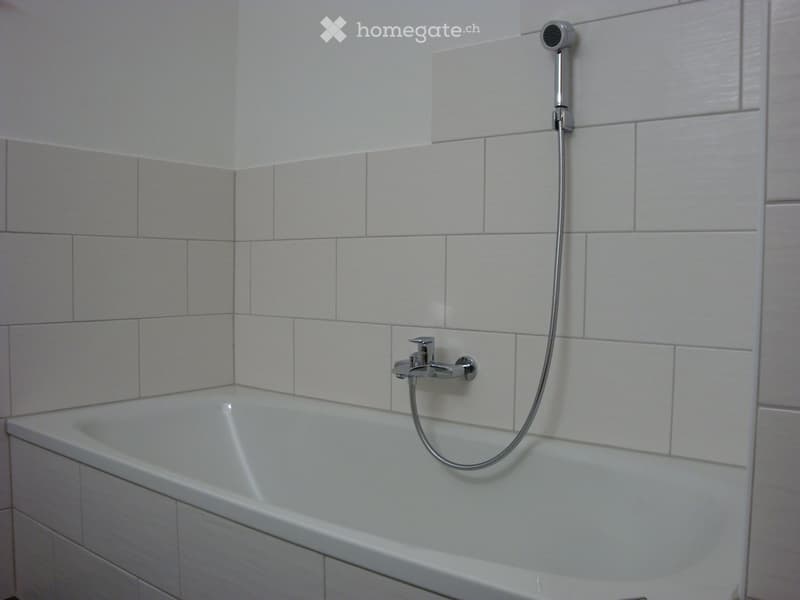 Bathtub with a handheld showerhead and faucet, white tiled walls.