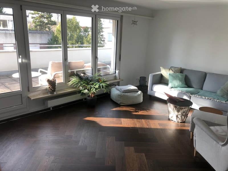 Modern living room with wooden flooring, large windows, grey sofa, coffee table, and potted plant.