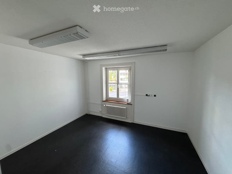 Empty room with white walls, dark flooring, a window with a small wooden sill, and a radiator below the window.