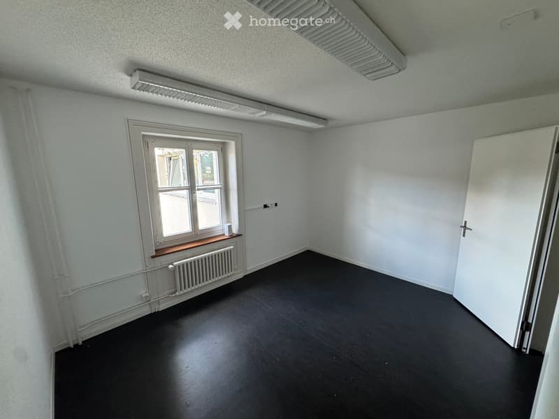 Empty room with white walls, dark flooring, a window with a radiator below, and a door on the right side.