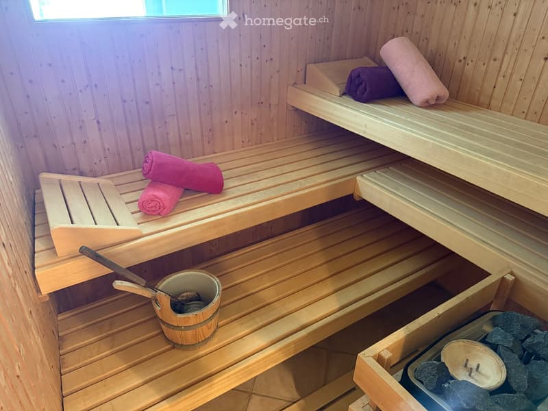 Wooden sauna with multiple benches, towels, a wooden bucket, and a wooden paddle for stirring water.