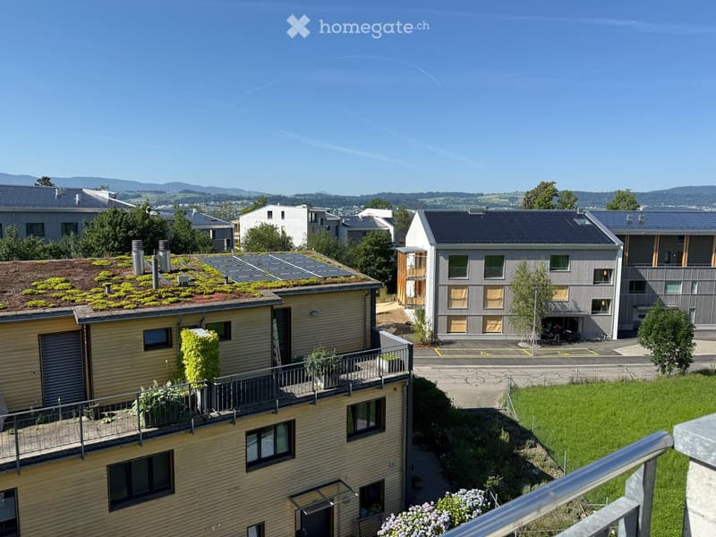 A modern residential complex with multiple buildings, green roofs, balconies, and surrounding greenery.