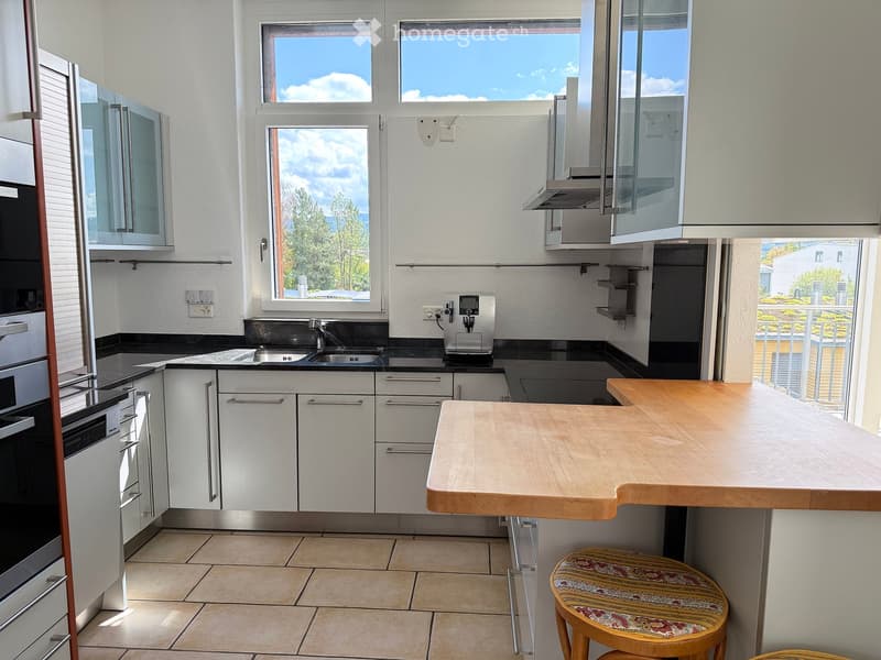 Modern kitchen with white cabinets, stainless steel appliances, a wooden island, and a small stool.