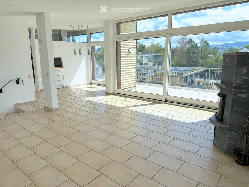Bright, open living space with large windows and sliding doors leading to a balcony, tiled floor, fireplace, and a small screen on a stand.