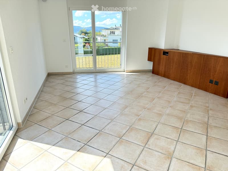Empty room with tiled floor, white walls, and a sliding glass door leading to a balcony with a view of the landscape.