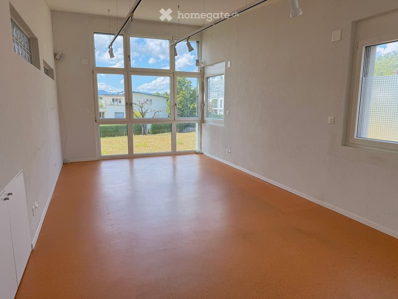Empty room with light wooden flooring, large windows, and white walls. No furniture or equipment present.