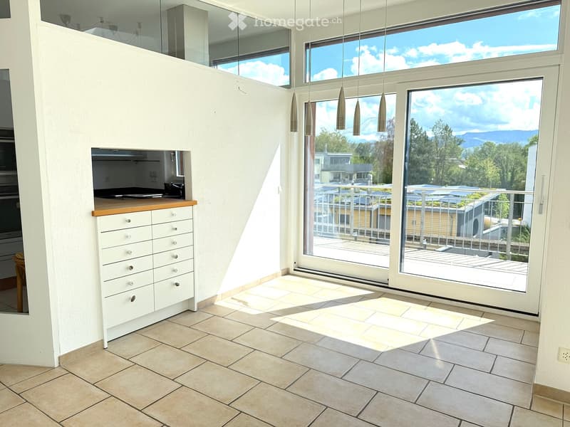 Bright, modern room with large windows offering a scenic view, a white cabinet with drawers, and pendant lights hanging from the ceiling.