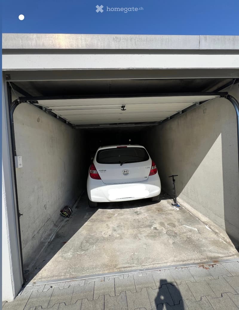 Underground parking space with a white car parked inside, concrete walls, and a raised ceiling.