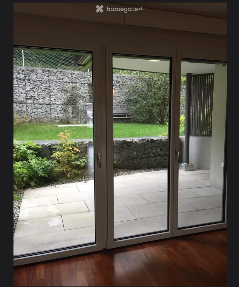 Sliding glass doors open to a paved patio area with a stone wall and garden visible outside.