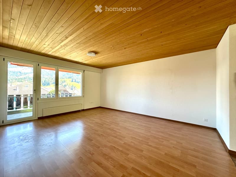 Empty room with wooden flooring, white walls, and large windows offering a view of the outdoors.