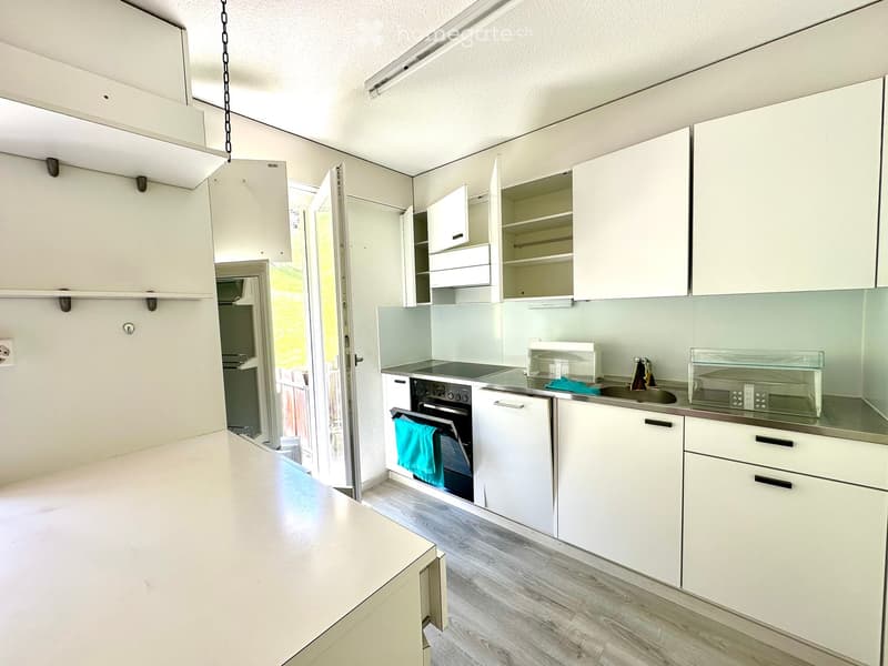 Modern kitchen with white cabinets, stainless steel appliances, and a light wooden floor.