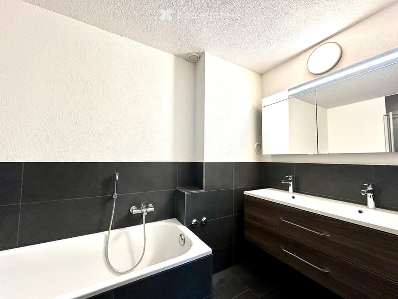 Modern bathroom with a bathtub, double sink, large mirror, and sleek fixtures.