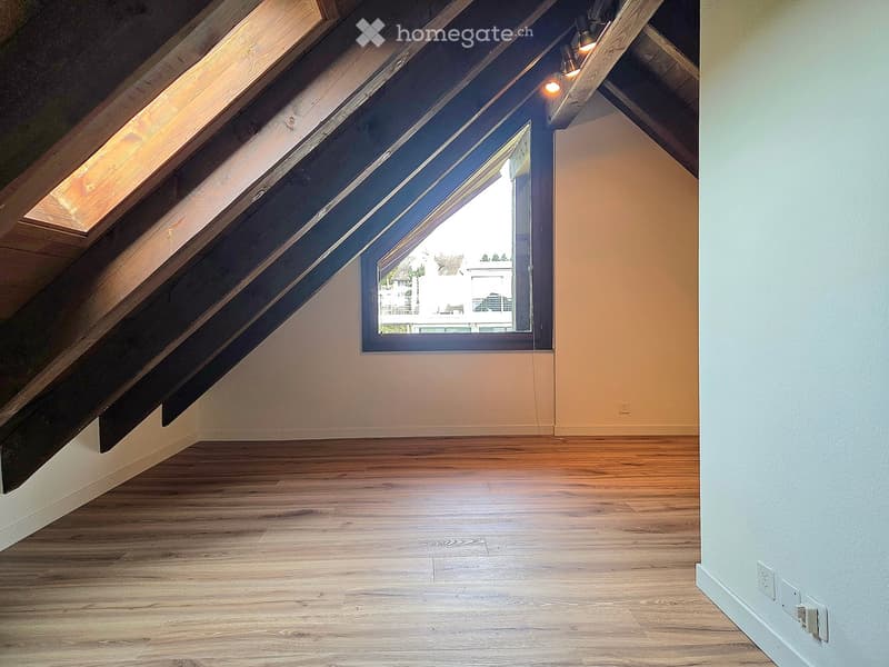 Empty attic room with wooden flooring, exposed wooden beams, skylight windows, and modern light fixtures.
