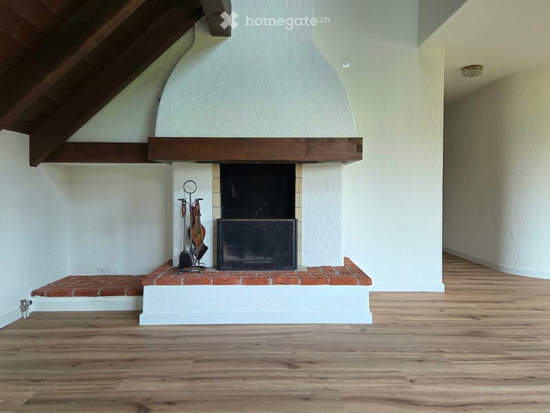 Empty room with wooden flooring and a fireplace with a wooden mantel and brick base. The fireplace includes a black metal grate and a set of fire tools placed beside it.