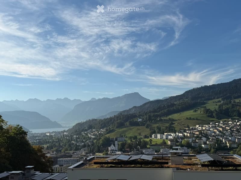 Panoramic view of a town nestled in a valley surrounded by mountains, with solar panels on the foreground roof.