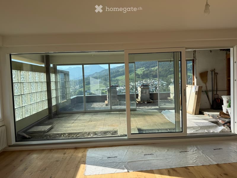Empty room with wooden flooring, large sliding glass doors leading to a balcony with a scenic mountain view.