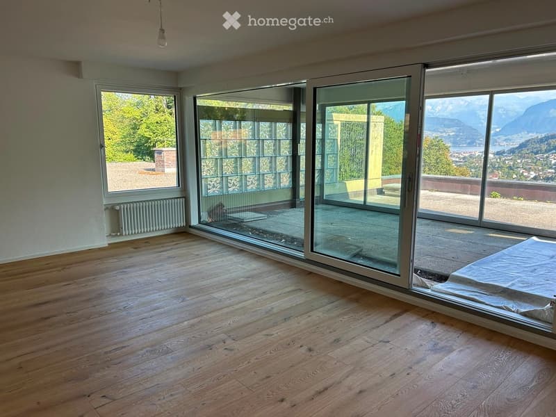 Empty room with wooden flooring, large glass sliding doors leading to a balcony, and a scenic mountain view.