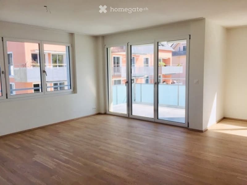 Empty room with wooden flooring, large windows, and sliding glass doors leading to a balcony.