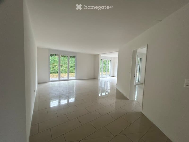 Empty room with white walls, tiled floor, large sliding glass doors leading to an outdoor area, and a visible doorway to another room.