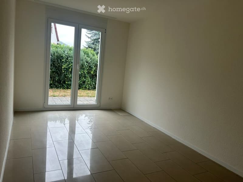 Empty room with tiled floor, large sliding glass door leading to outdoor area, white walls, and visible electrical outlet.