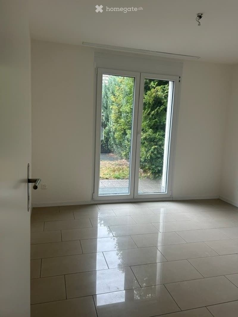 Empty room with tiled floor, large sliding glass door leading to outdoor area, white walls, and a visible door handle on the left side.