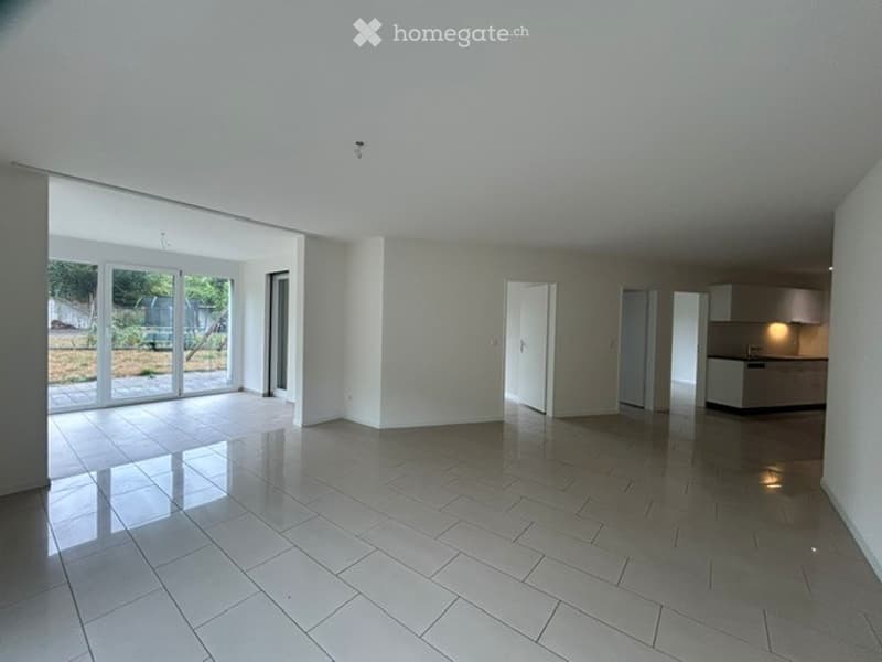 Open-plan unfurnished space with large glass sliding doors leading to an outdoor area, white tiled flooring, and neutral-colored walls.
