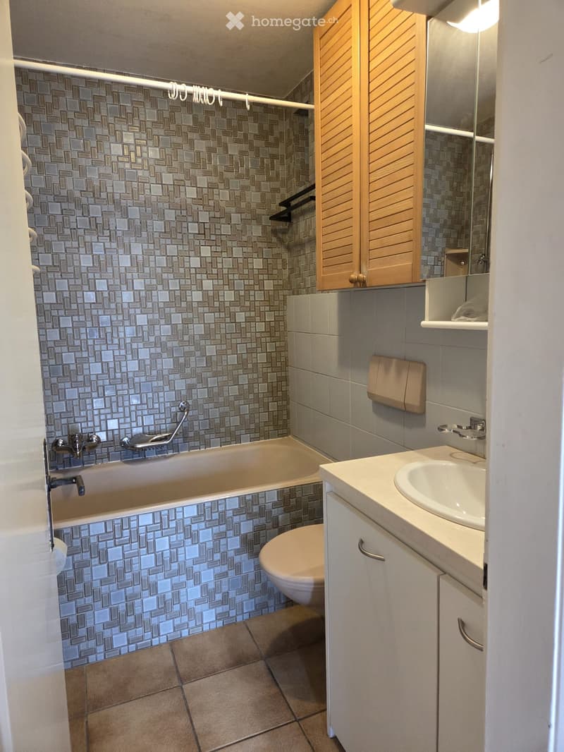 Bathroom with bathtub, toilet, sink, cabinets, tiled wall and floor, mirror, towel holder, and grab bar.