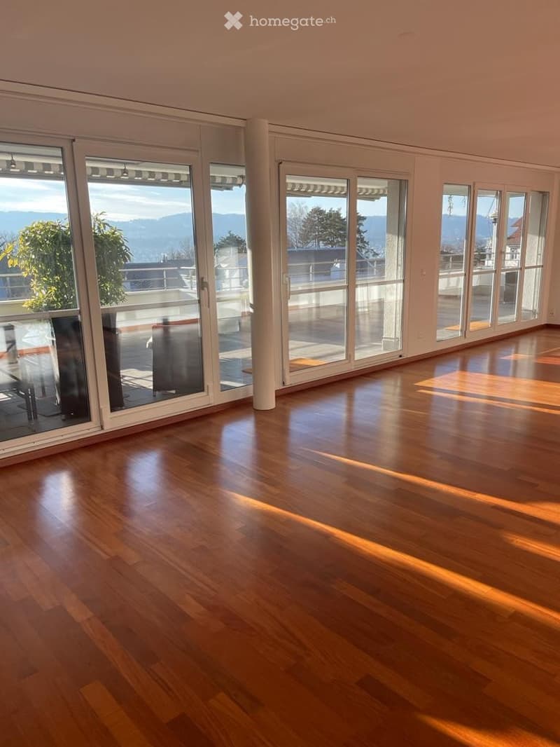 Bright, empty room with large glass sliding doors leading to a balcony, wooden flooring, and a scenic mountain view.