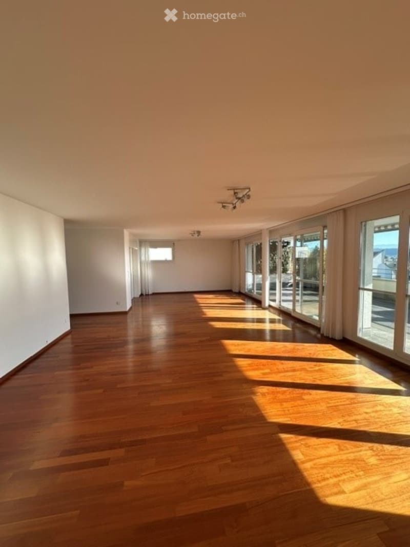 Empty room with wooden flooring, white walls, large windows with curtains, and recessed lighting.