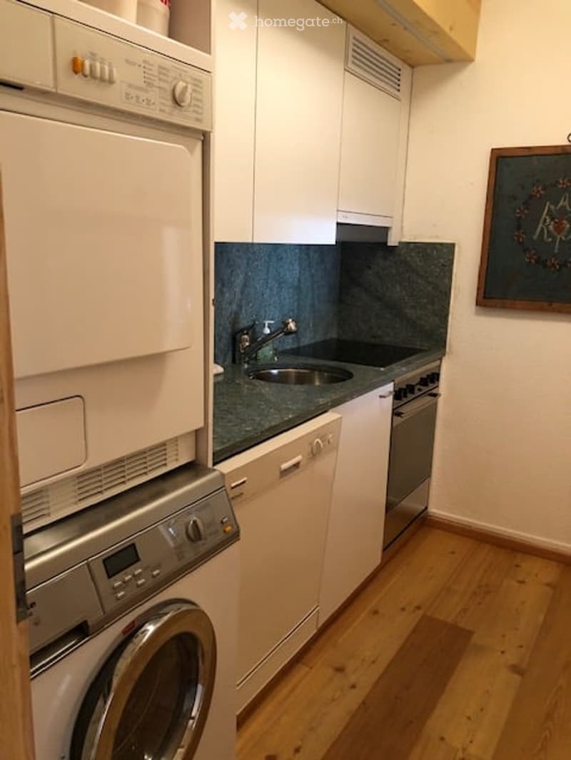 Compact kitchen with white cabinets, granite countertops, stainless steel appliances, and a washing machine.